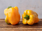Two blocky, bright yellow Golden Cal Wonder sweet peppers resting on a rustic wooden surface.