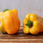 Two blocky, bright yellow Golden Cal Wonder sweet peppers resting on a rustic wooden surface.