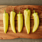 Five pale yellow Hungarian Hot Wax peppers arranged vertically on a rustic wooden cutting board.