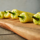 Pale yellow Hungarian Hot Wax peppers lined up on a wooden cutting board.