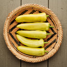 Five pale yellow Hungarian Hot Wax peppers arranged in a woven bamboo basket on a wooden surface.
