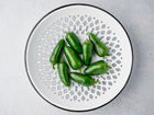 Glossy green Jalapeño peppers arranged on a decorative white and black patterned ceramic plate.