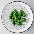 Glossy green Jalapeño peppers arranged on a decorative white and black patterned ceramic plate.