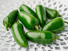 Glossy green Jalapeño peppers arranged in a white decorative lattice bowl.