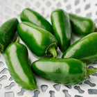 Glossy green Jalapeño peppers arranged in a white decorative lattice bowl.