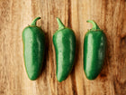 Three glossy, dew-covered green Jalapeño peppers arranged in a row on a rustic wooden surface.