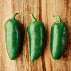 Three glossy, dew-covered green Jalapeño peppers arranged in a row on a rustic wooden surface.