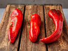Three long, tapered Marconi Red sweet peppers with smooth, glossy red skin resting on a rustic wooden crate.