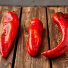 Three long, tapered Marconi Red sweet peppers with smooth, glossy red skin resting on a rustic wooden crate.