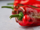 Close-up of long, tapered Marconi Red sweet peppers with smooth, glossy red skin and green stems on a light surface.