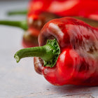 Close-up of long, tapered Marconi Red sweet peppers with smooth, glossy red skin and green stems on a light surface.