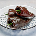 Three ripe, chocolate-brown Mulato Isleño peppers resting in a white, lattice-patterned enamel bowl.