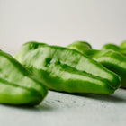 Fresh green Padron peppers with wrinkled skin arranged on a light textured surface.