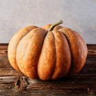 A flattened, tan Musquée de Provence pumpkin with deep ribs sitting on a rustic wooden table.