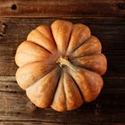 Top-down view of a tan, deeply ribbed Musquee de Provence pumpkin resting on a rustic dark wooden surface.