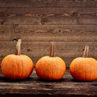 Three round orange Small Sugar Pie pumpkins lined up on a rustic dark wood surface against a wooden plank background.