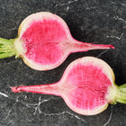 Two halved Watermelon radishes showing vibrant pink centers and pale green skin on a dark marble surface.