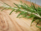 Fresh green rosemary sprigs with needle-like leaves resting on a rustic wooden cutting board.