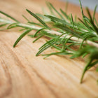 Fresh green rosemary sprigs with needle-like leaves resting on a rustic wooden cutting board.