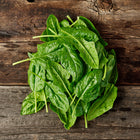 Freshly harvested Bloomsdale spinach leaves with dark green, crinkled texture resting on a rustic wooden surface.
