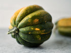 Dark green, ribbed Table Queen acorn squash with golden patches resting on a grey surface.