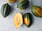 Table Queen acorn squash with dark green ribbed skin and one halved fruit showing golden flesh and seeds.