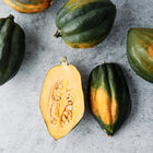 Table Queen acorn squash with dark green ribbed skin and one halved fruit showing golden flesh and seeds.