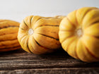 Close-up of oblong Delicata winter squash with cream skin and green stripes resting on a rustic wooden surface.