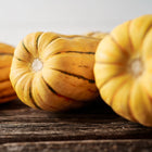 Close-up of oblong Delicata winter squash with cream skin and green stripes resting on a rustic wooden surface.