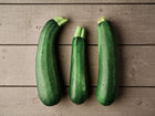 Three dark green Black Beauty zucchini squash arranged on a rustic grey wooden surface.
