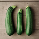 Three dark green Black Beauty zucchini squash arranged on a rustic grey wooden surface.
