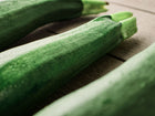 Three glossy, dark green Black Beauty zucchini squash resting on a rustic wooden surface.