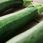 Three glossy, dark green Black Beauty zucchini squash resting on a rustic wooden surface.