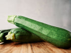 Two dark green, glossy Black Beauty zucchini squash resting on a wooden cutting board.