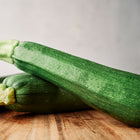 Two dark green, glossy Black Beauty zucchini squash resting on a wooden cutting board.