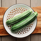 Two Cocozelle zucchini with light green stripes resting on a white decorative colander atop a wooden board.