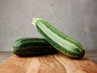 Two Cocozelle zucchini with dark and light green stripes resting on a wooden cutting board.