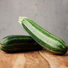 Two Cocozelle zucchini with dark and light green stripes resting on a wooden cutting board.