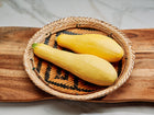 Two Early Prolific Straightneck summer squash in a woven basket on a wooden board.