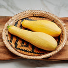 Two Early Prolific Straightneck summer squash in a woven basket on a wooden board.
