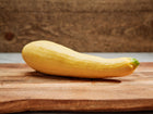 A single Early Prolific Straightneck summer squash with smooth, lemon-yellow skin resting on a wooden cutting board.