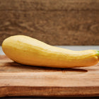 A single Early Prolific Straightneck summer squash with smooth, lemon-yellow skin resting on a wooden cutting board.
