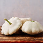 Three pale, scalloped Early White Bush Scallop squash resting on a rustic wooden surface.