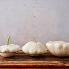 Three Early White Bush Scallop summer squash with pale, scalloped edges arranged on a rustic wooden surface.