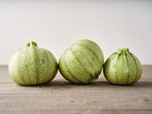 Three round, pale green speckled Ronde de Nice summer squash sitting on a rustic wooden surface.