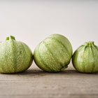 Three round, pale green speckled Ronde de Nice summer squash sitting on a rustic wooden surface.