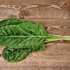 A bunch of Fordhook Giant Swiss chard with dark green crinkled leaves and thick white stems tied on a wooden surface.