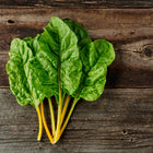 Freshly harvested Oriole Orange Swiss chard with glossy green leaves and bright orange stems on a rustic wood background.