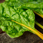 Oriole Orange Swiss chard leaves with glossy green textures and vibrant orange stems resting on a rustic wooden surface.