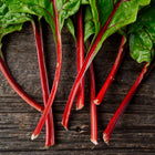 Ruby Red Swiss chard leaves with vibrant crimson stems laid out on a dark, weathered wooden surface.